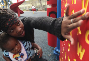 An adult pointing out letters on a playground to their child.