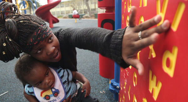 An adult pointing out letters on a playground to their child.