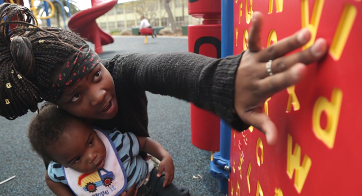 An adult pointing out letters on a playground to their child.