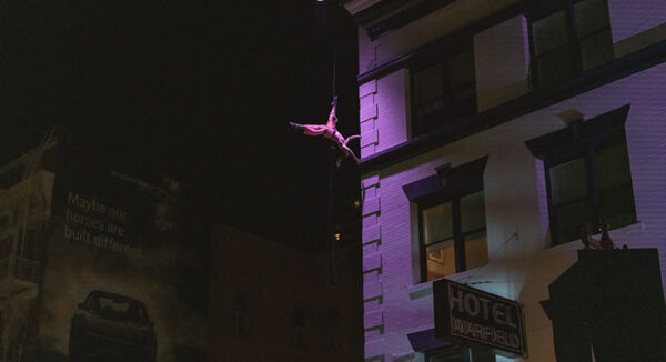 An aerial dancer shown upside down, mid-air alongside a building in San Francisco.