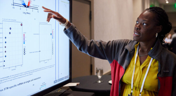Someone pointing to a screen, sharing their research during a digital poster session.