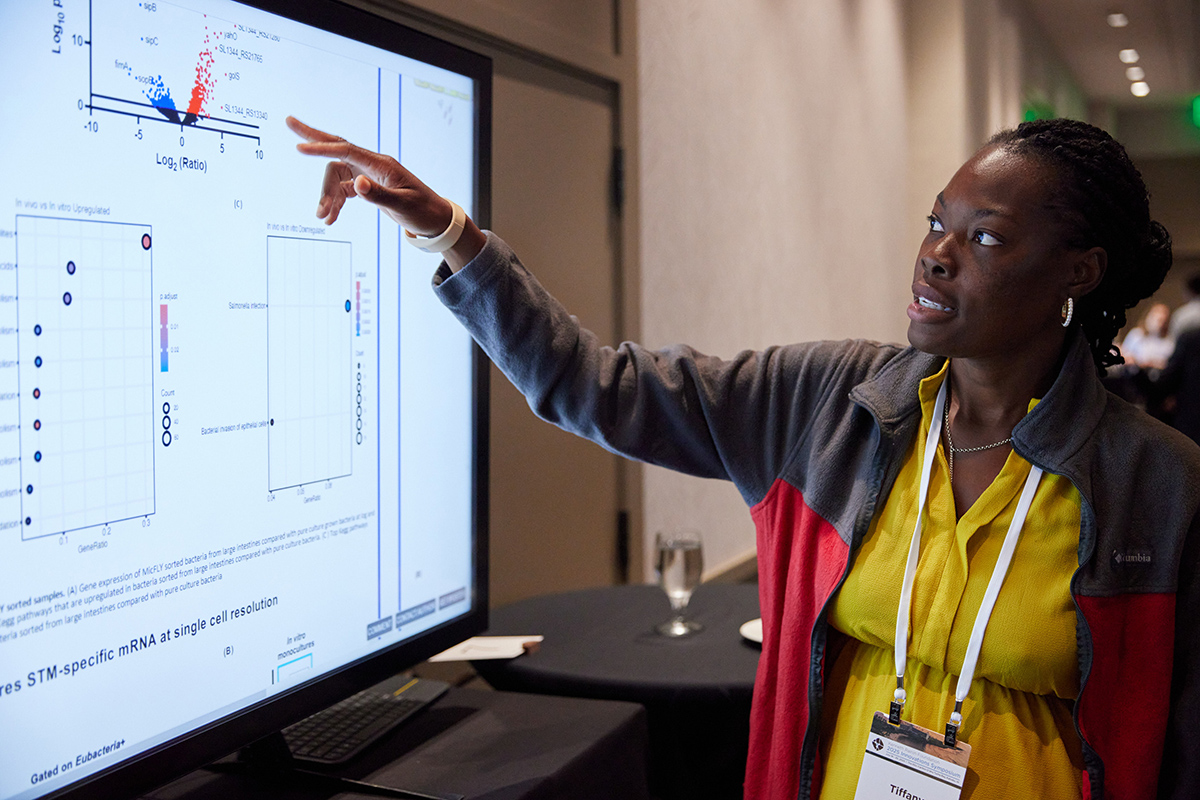 Someone pointing to a screen, sharing their research during a digital poster session.