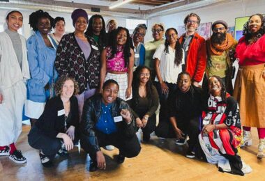 Eighteen people pose together for a group photo, some standing and some crouching.