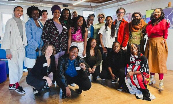 Eighteen people pose together for a group photo, some standing and some crouching.