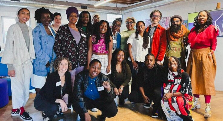 Eighteen people pose together for a group photo, some standing and some crouching.