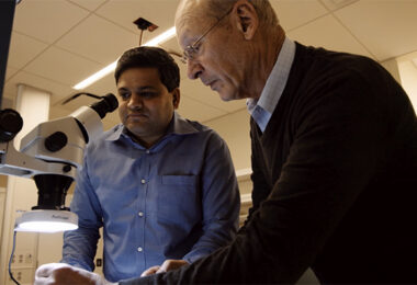 Dr. Steve Axelrod and Dr. Anand Navalgund working in the lab, using a microscope.
