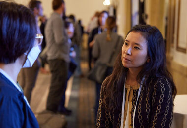 Dr. Julie Saiki speaking with another Symposium attendee while sharing her research in a digital poster session.
