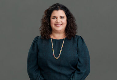 Image of Lorena Gomez-Barris, a Latina woman with long, curly black hair. She’s smiling at the camera, wearing a green blouse and long necklace.