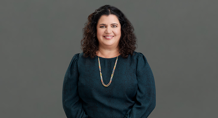 Image of Lorena Gomez-Barris, a Latina woman with long, curly black hair. She’s smiling at the camera, wearing a green blouse and long necklace.