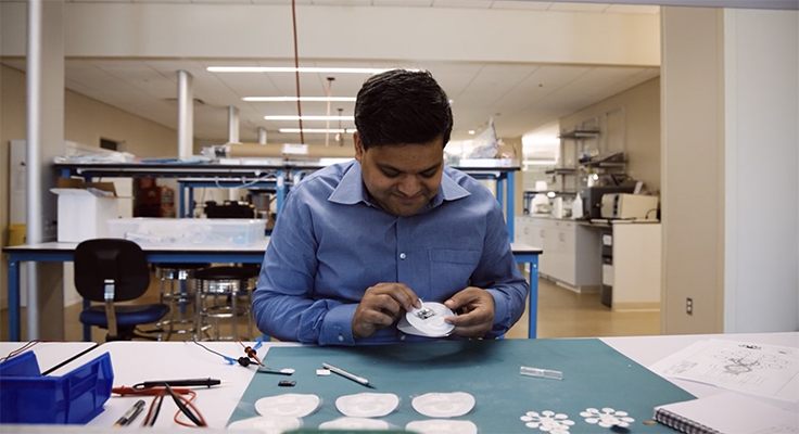 Dr. Anand Navalgund in a lab holding G-Tech Medical's novel wireless patch.