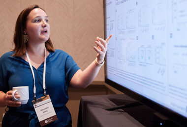 A scientist pointing at their research findings on a large screen.