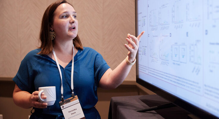 A scientist pointing at their research findings on a large screen.