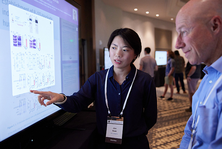 A person points at visual charts on a digital screen while a second person listens closely.