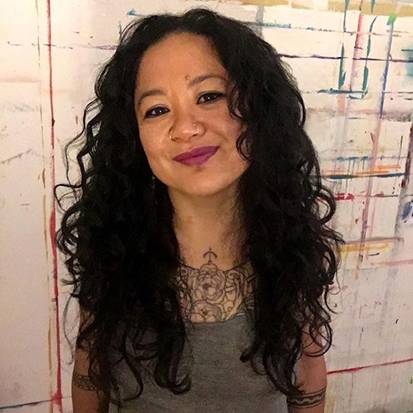 Carpio, a Filipina woman with long curly black hair, in front of her studio painted wall.