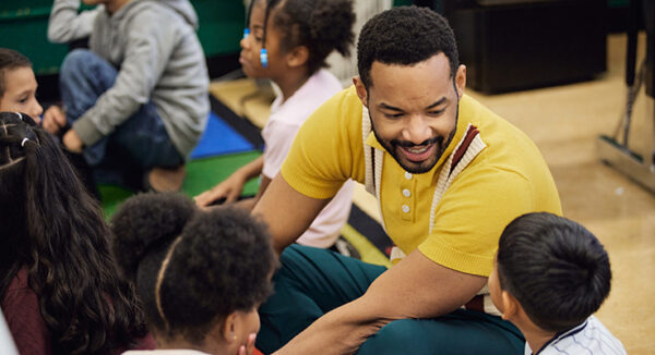 An educator sitting on the floor, in conversation with students.