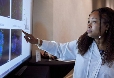 Someone pointing at research images on a screen during a digital poster presentation.