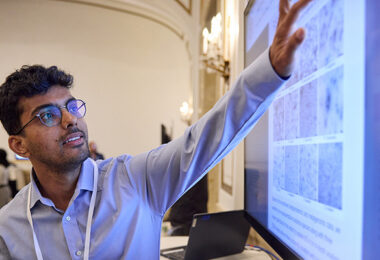 A person pointing at a large screen displaying a research poster.