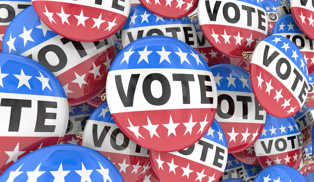 A close crop on a pile of buttons that say "VOTE" and are red, white and blue striped with white stars