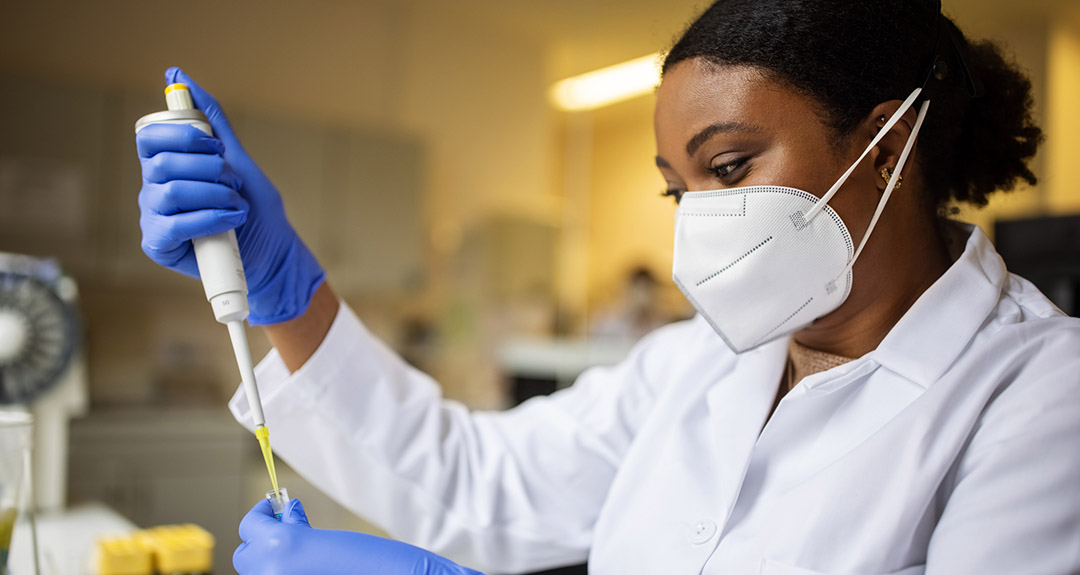 a lab workers in a white lab coat and medical mask uses a pipette