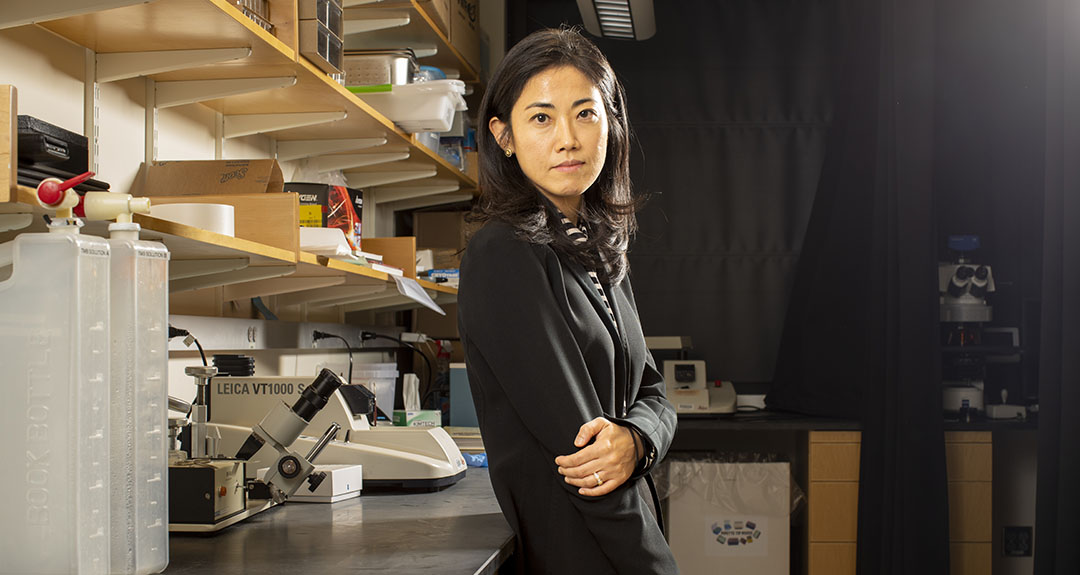 A person gazes intently at the camera while standing in a scientific lab.