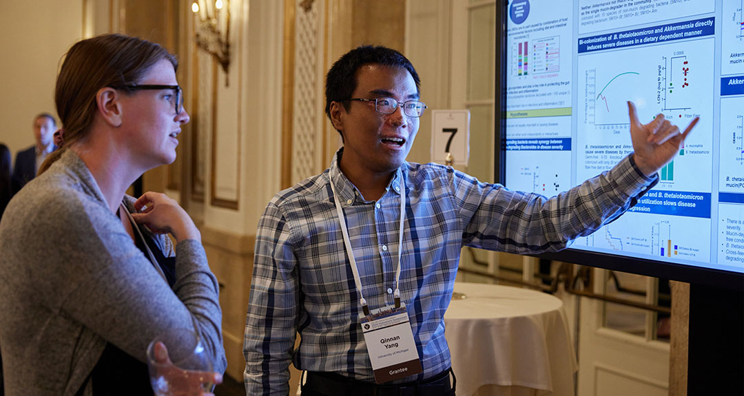A person points at charts on a screen while another person listens intently.
